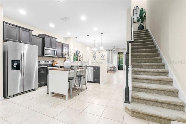 kitchen featuring light tile patterned floors, a breakfast bar area, a peninsula, a kitchen island, and appliances with stainless steel finishes