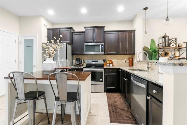 kitchen featuring light tile patterned floors, tasteful backsplash, appliances with stainless steel finishes, a breakfast bar, and a sink