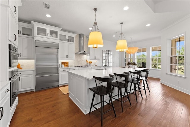 kitchen with a spacious island, hanging light fixtures, white cabinetry, stainless steel built in refrigerator, and wall chimney exhaust hood