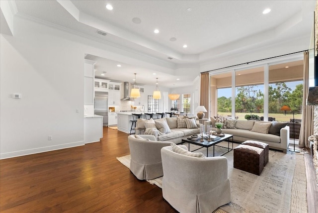 living area with dark wood-style floors, a tray ceiling, recessed lighting, ornamental molding, and baseboards