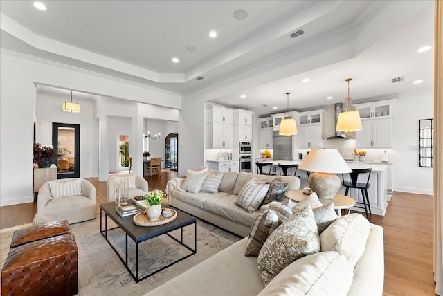 living area with a tray ceiling, light wood-style flooring, visible vents, and baseboards