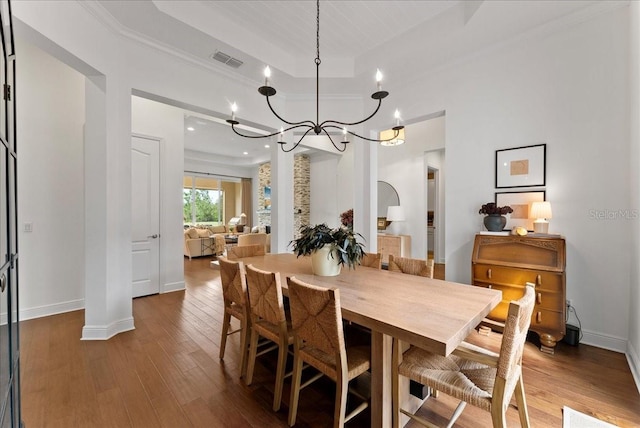 dining area with a tray ceiling, wood-type flooring, visible vents, a chandelier, and baseboards