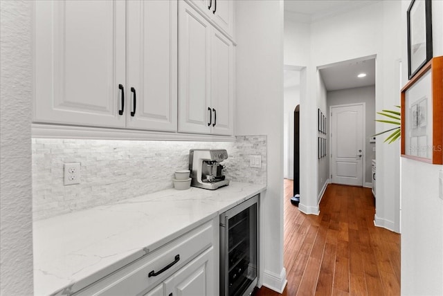 bar featuring arched walkways, hardwood / wood-style flooring, beverage cooler, baseboards, and tasteful backsplash