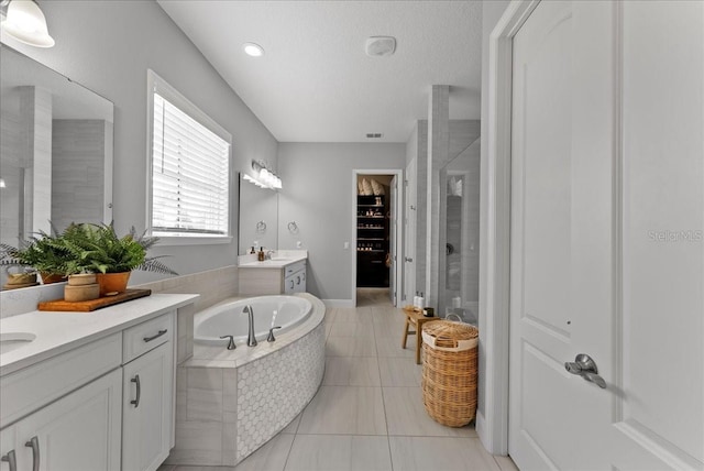 bathroom with a walk in closet, two vanities, a sink, a shower stall, and tile patterned flooring