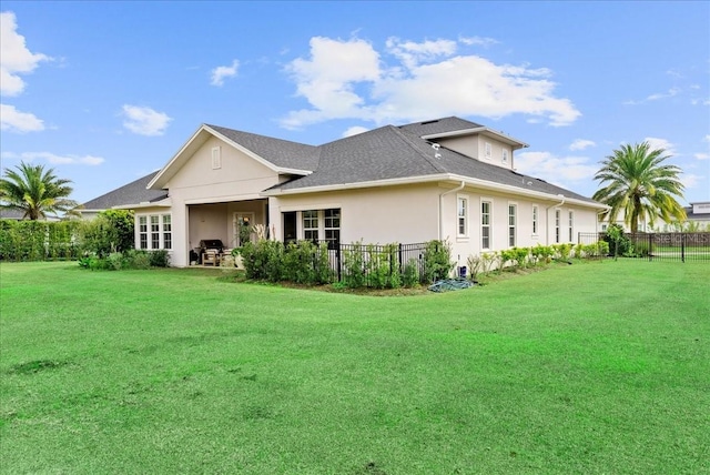 rear view of property featuring a yard, a shingled roof, fence, and stucco siding