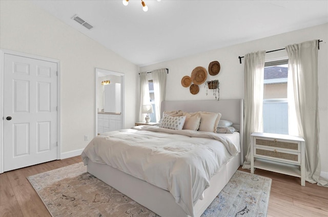 bedroom featuring lofted ceiling, ensuite bathroom, visible vents, baseboards, and light wood-type flooring