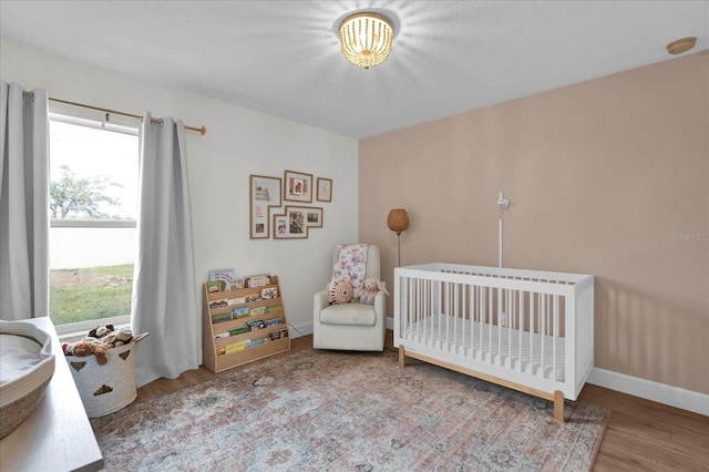 bedroom featuring a nursery area, baseboards, and wood finished floors