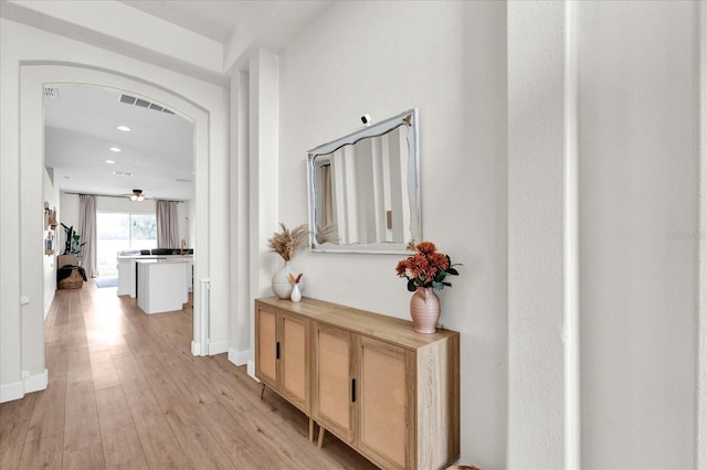 hall with arched walkways, light wood-style flooring, recessed lighting, visible vents, and baseboards