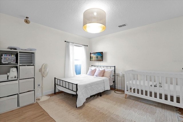 bedroom featuring a textured ceiling, wood finished floors, visible vents, and baseboards