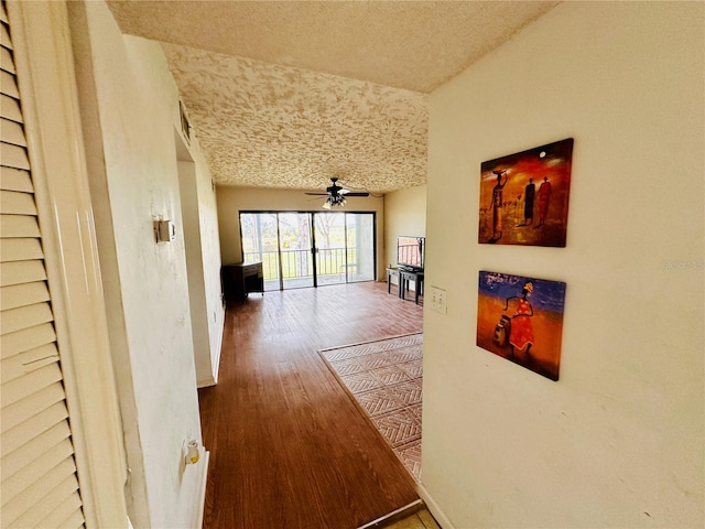 corridor with a textured ceiling, wood finished floors, and baseboards