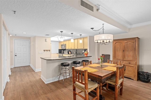 dining area featuring light wood finished floors, baseboards, visible vents, and a textured ceiling