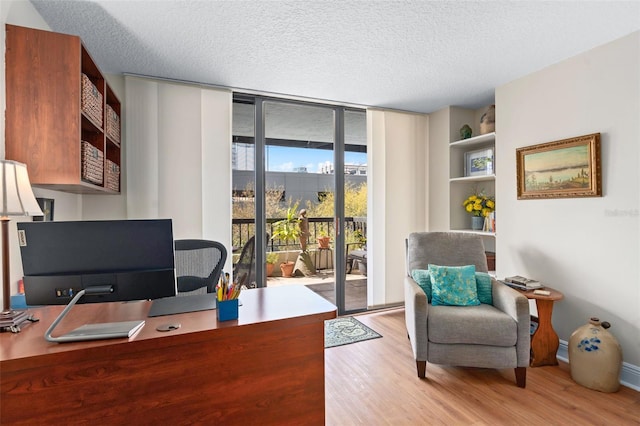 office with light wood-type flooring, expansive windows, baseboards, and a textured ceiling