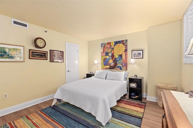 bedroom featuring a textured ceiling, wood finished floors, visible vents, and baseboards