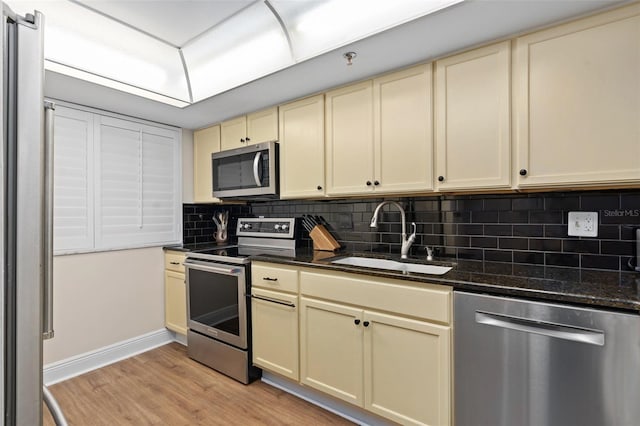 kitchen featuring a sink, cream cabinets, stainless steel appliances, light wood-style floors, and backsplash