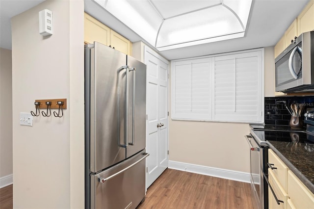 kitchen with stainless steel appliances, cream cabinetry, light wood finished floors, and tasteful backsplash