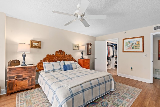 bedroom with wood finished floors, a closet, a walk in closet, and baseboards