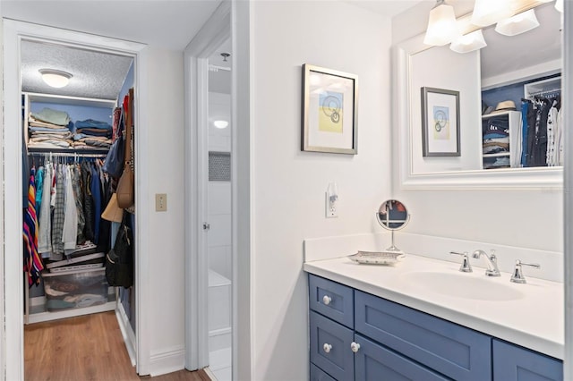 bathroom featuring a textured ceiling, a spacious closet, wood finished floors, and vanity