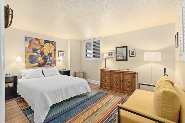 bedroom featuring a textured ceiling, baseboards, and wood finished floors