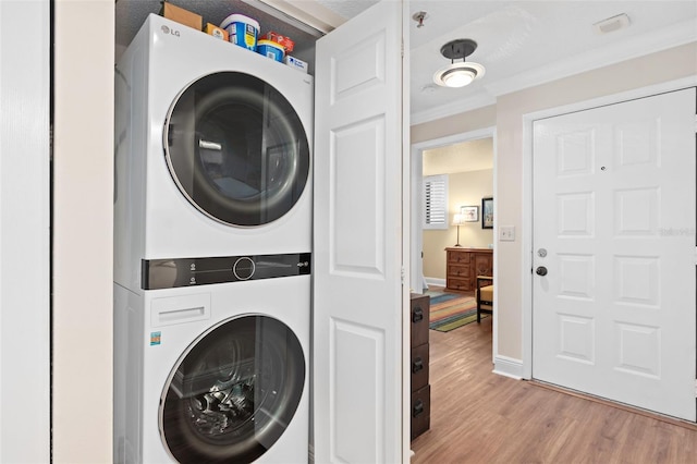 washroom with light wood-style flooring, laundry area, baseboards, stacked washing maching and dryer, and crown molding