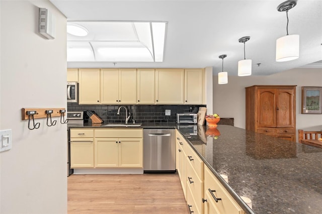 kitchen with tasteful backsplash, cream cabinets, appliances with stainless steel finishes, light wood-style floors, and a sink