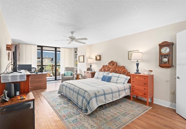 bedroom with a textured ceiling, light wood finished floors, expansive windows, and access to exterior