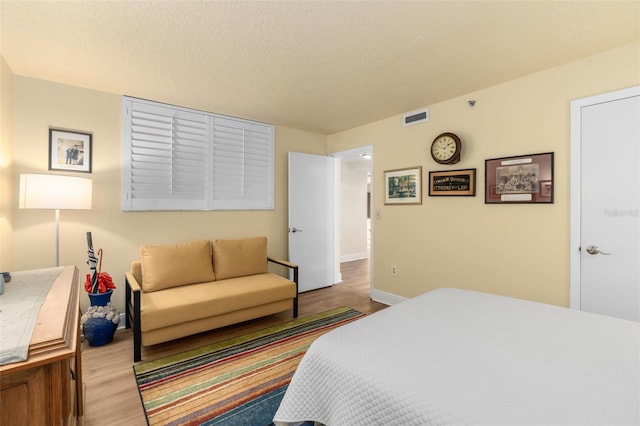 bedroom with baseboards, a textured ceiling, visible vents, and wood finished floors