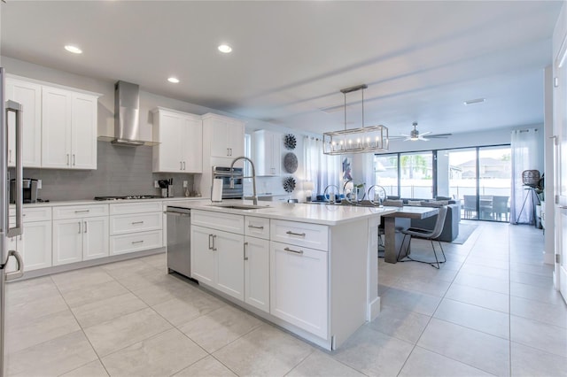 kitchen with a kitchen island with sink, white cabinetry, light countertops, wall chimney range hood, and decorative light fixtures