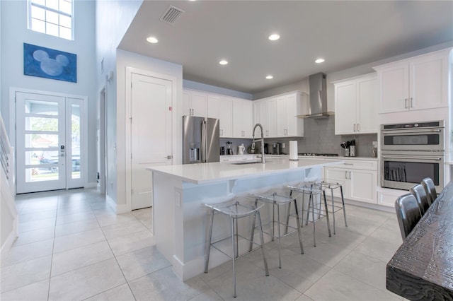 kitchen featuring stainless steel appliances, light countertops, wall chimney exhaust hood, and white cabinetry