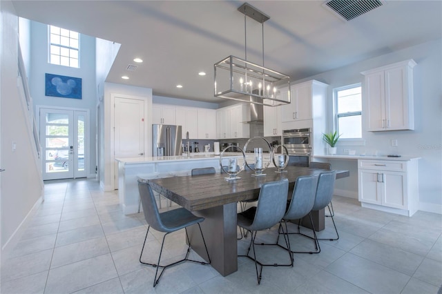 kitchen featuring a kitchen island with sink, stainless steel appliances, visible vents, white cabinets, and wall chimney range hood