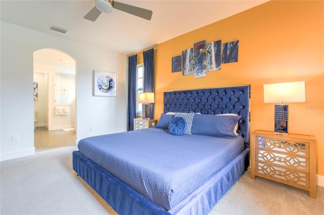 carpeted bedroom featuring arched walkways, visible vents, ensuite bathroom, a ceiling fan, and baseboards