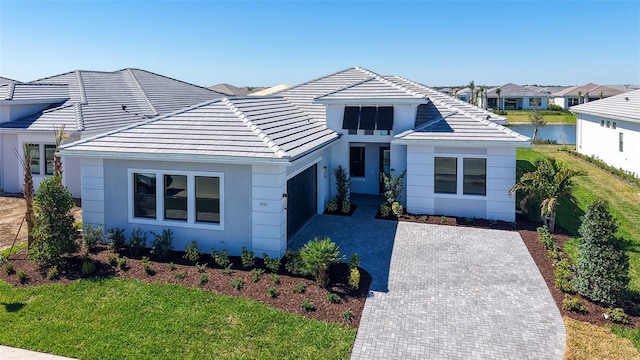 view of front of property with a water view, a tile roof, decorative driveway, stucco siding, and a front lawn