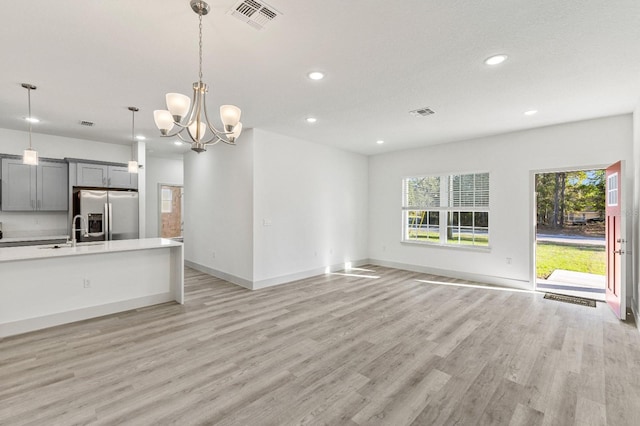 unfurnished living room featuring plenty of natural light, a sink, visible vents, and light wood-style floors