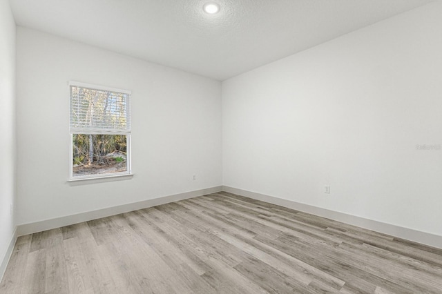 unfurnished room featuring light wood-type flooring, baseboards, and a textured ceiling