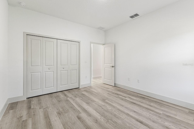 unfurnished bedroom with baseboards, a closet, visible vents, and wood finished floors