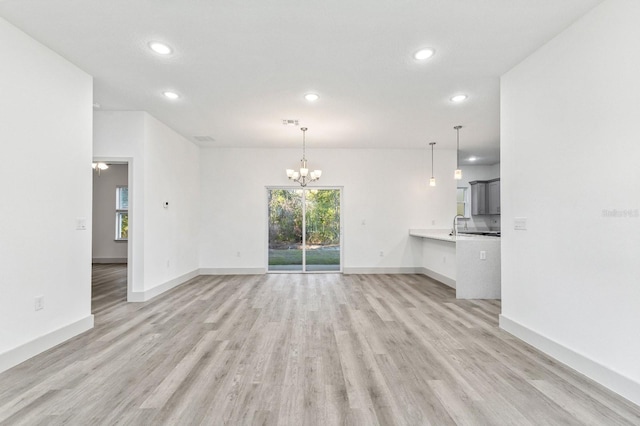 unfurnished living room with baseboards, light wood-style floors, recessed lighting, and an inviting chandelier