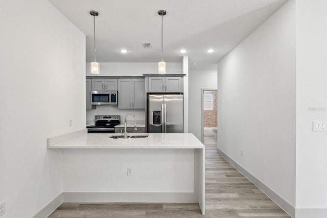 kitchen featuring stainless steel appliances, gray cabinets, a sink, and light wood-style flooring