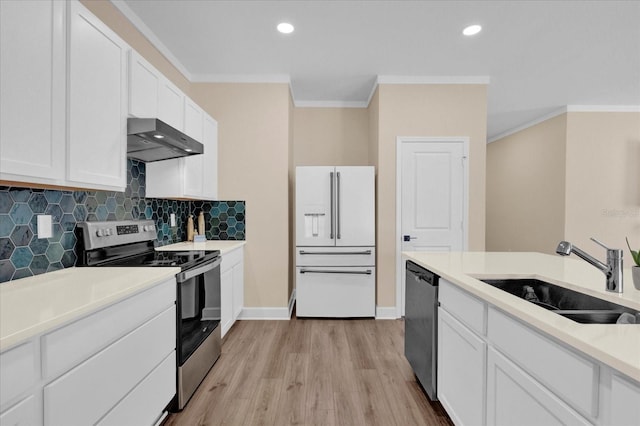 kitchen with appliances with stainless steel finishes, ornamental molding, white cabinets, a sink, and wall chimney exhaust hood