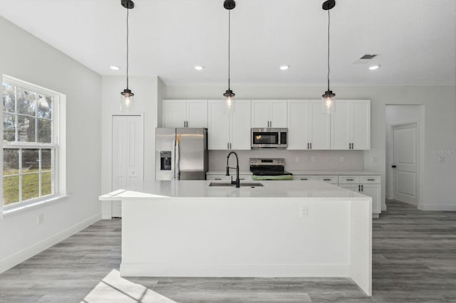 kitchen with appliances with stainless steel finishes, white cabinetry, a sink, and a center island with sink