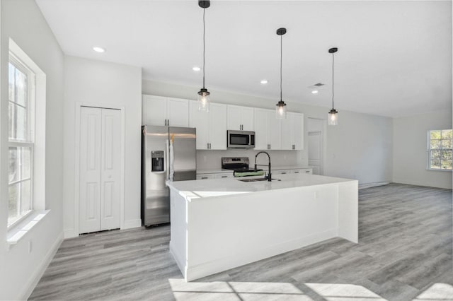 kitchen with a kitchen island with sink, stainless steel appliances, a sink, white cabinetry, and light countertops