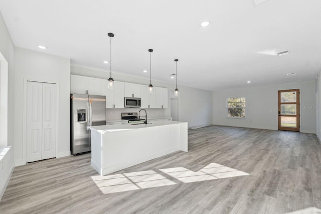 kitchen with a center island with sink, stainless steel appliances, light countertops, white cabinets, and a sink