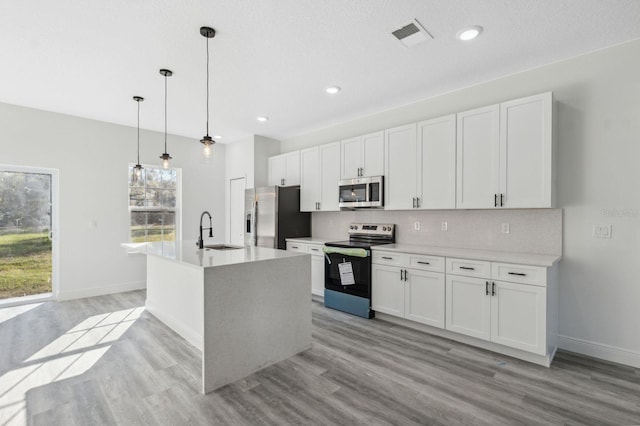 kitchen featuring a center island with sink, white cabinets, decorative backsplash, stainless steel appliances, and a sink