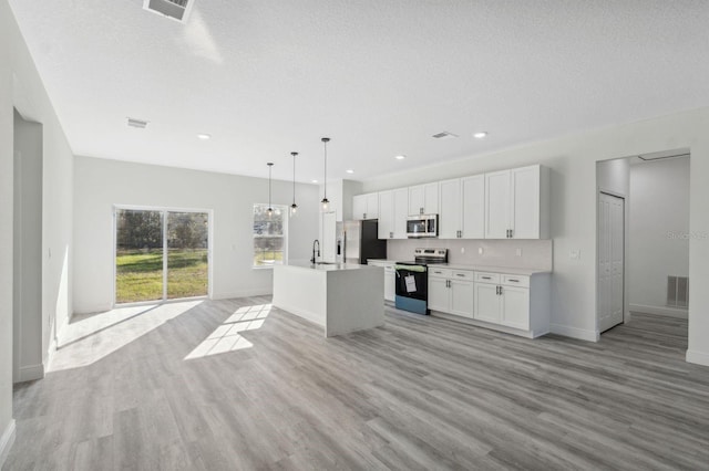 kitchen with visible vents, appliances with stainless steel finishes, open floor plan, a kitchen island with sink, and white cabinetry