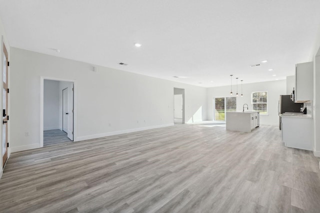 unfurnished living room featuring light wood finished floors, baseboards, visible vents, and a sink