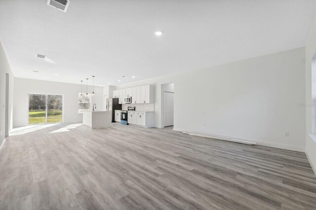 unfurnished living room featuring light wood-style flooring, recessed lighting, a sink, visible vents, and baseboards