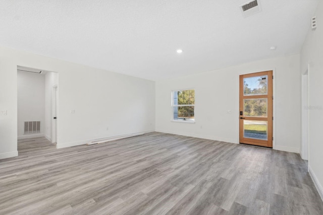 empty room with light wood finished floors, visible vents, and baseboards