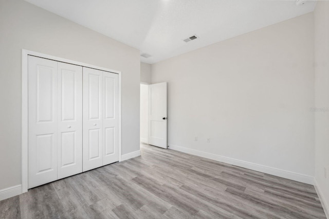 unfurnished bedroom with visible vents, a closet, baseboards, and wood finished floors