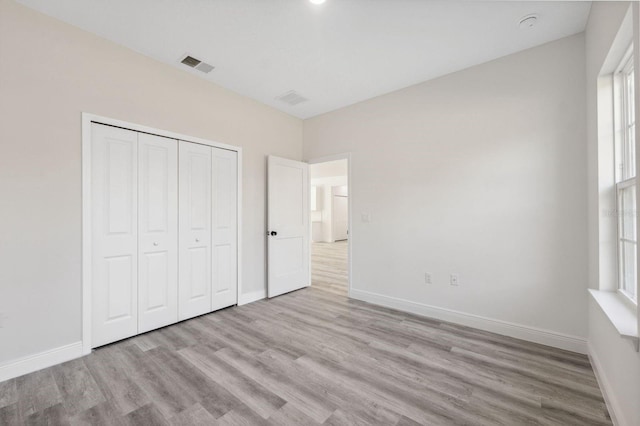 unfurnished bedroom featuring a closet, wood finished floors, visible vents, and baseboards