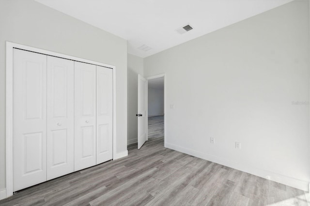 unfurnished bedroom with a closet, wood finished floors, visible vents, and baseboards