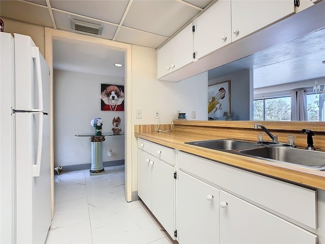 kitchen featuring visible vents, light countertops, freestanding refrigerator, white cabinets, and a sink