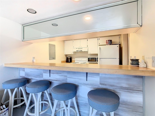 kitchen with under cabinet range hood, a breakfast bar area, electric panel, a peninsula, and white appliances